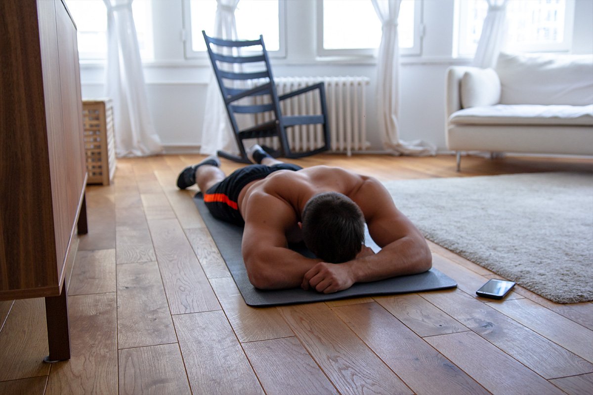 Ripped man, lying in the mat in the apartment, hans supporting his head, mobile phone lying nex to him.