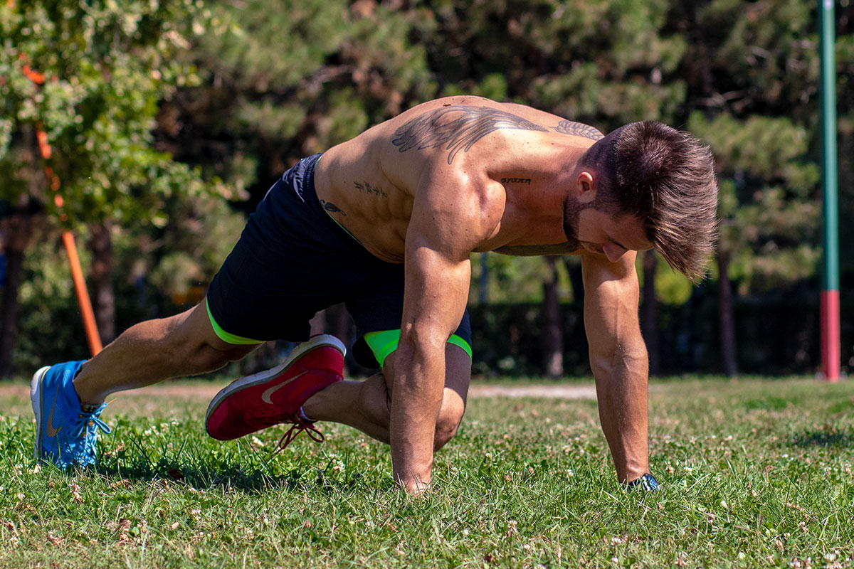 Man in fully extended push up position, left leg raised, left knee reaching for rigth elbow