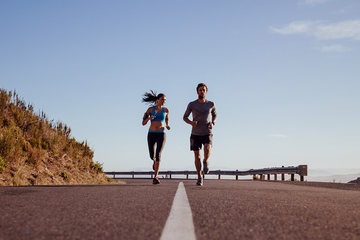 man and woman in sports equipement running on empy highway